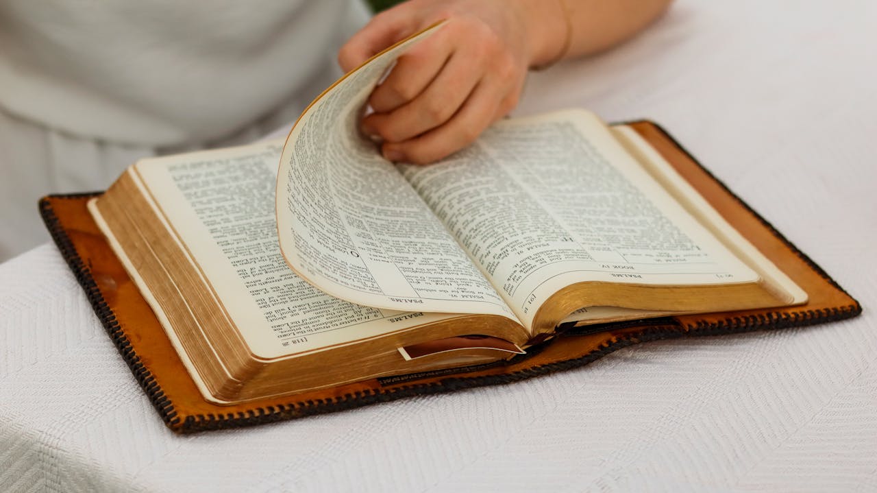 A person's hand turning pages of an open Bible, creating a peaceful study scene.