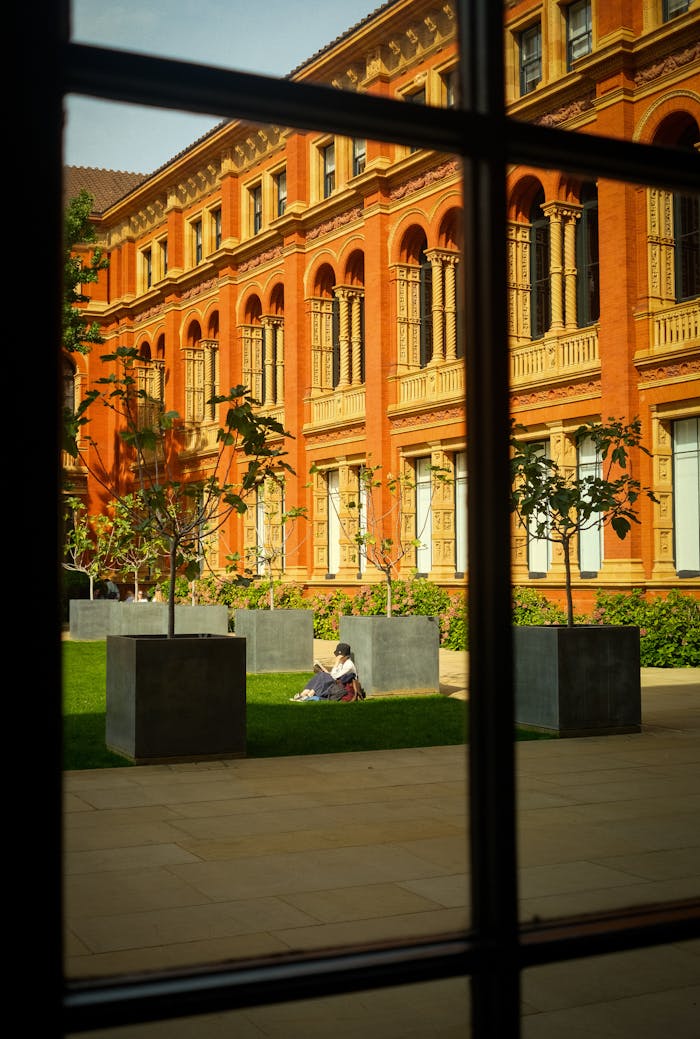 A person enjoys a sunny day in a historic courtyard with red brick architecture.